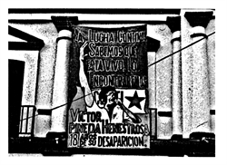 [ai] A black and white image of a banner on a building, featuring a raised fist and text in Spanish. The banner commemorates Victor Jara, mentioning his disappearance and the ongoing struggle for justice.